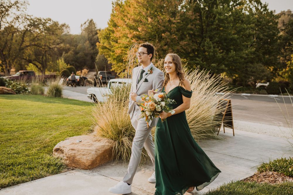 Elegant couple in grey and emerald attire walking through an autumn landscape.