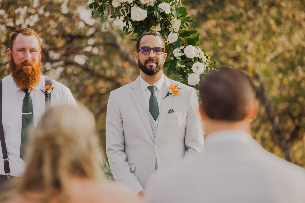 Wedding party in light gray suits and floral boutonnieres standing together outdoors.
