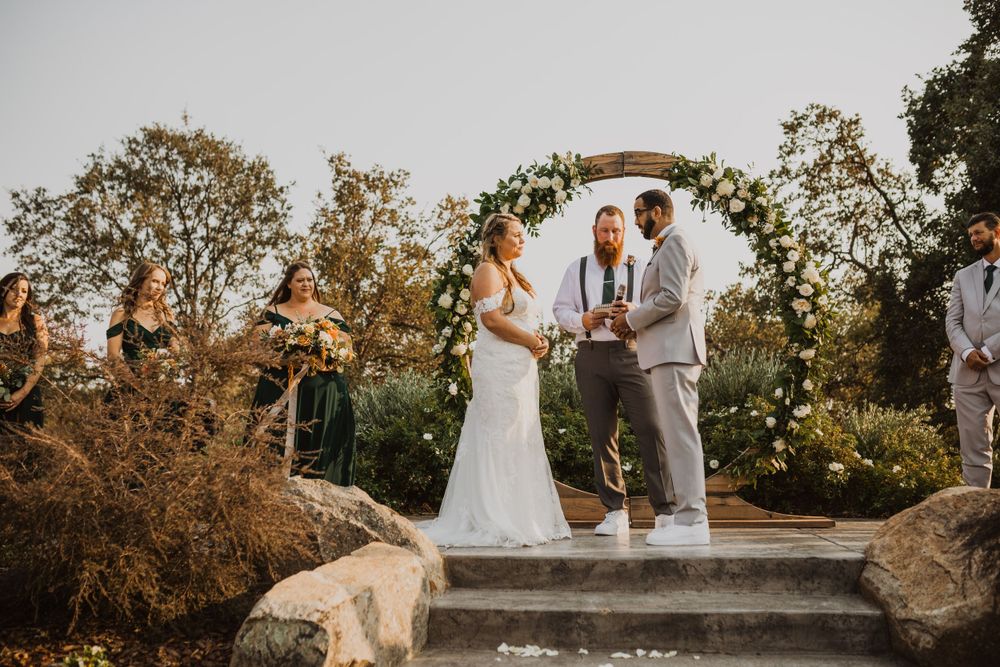 Outdoor wedding ceremony with guests seated on white chairs under autumn trees.