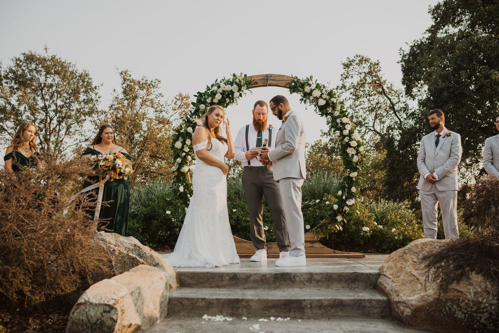 Outdoor wedding ceremony with guests watching couple exchange vows under natural lighting.