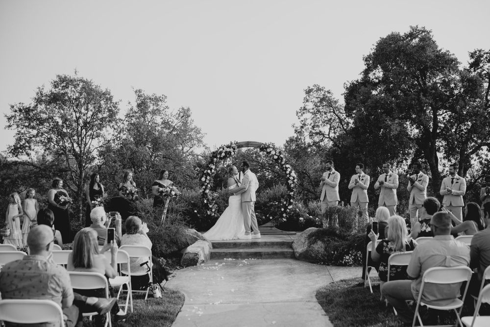 Wedding guests seated in white chairs on a grassy lawn during an outdoor ceremony at sunset.