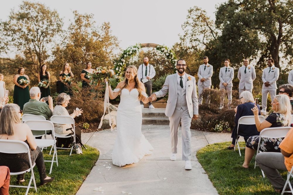 Wedding party and guests gathered on lawn with white chairs during outdoor celebration.