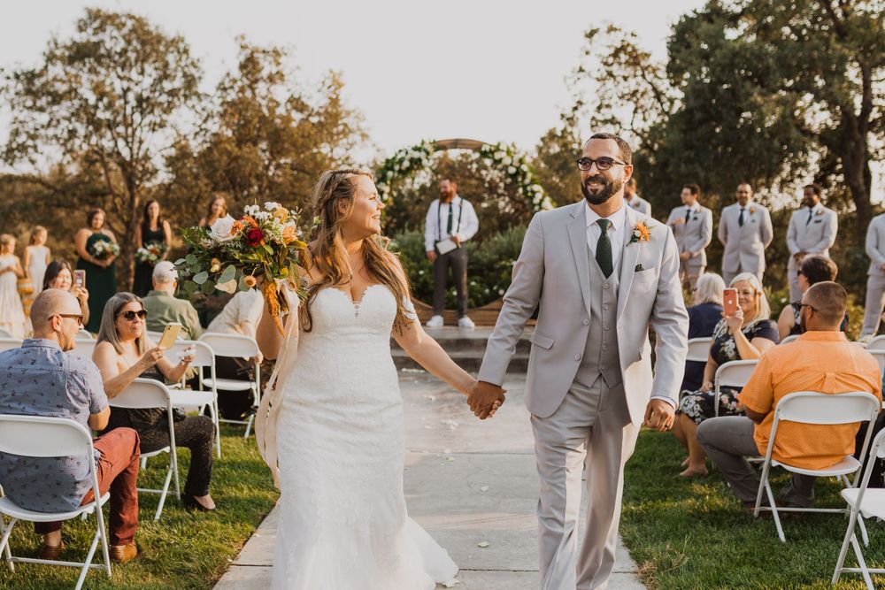 Outdoor wedding ceremony with guests seated in white chairs on a grassy lawn.