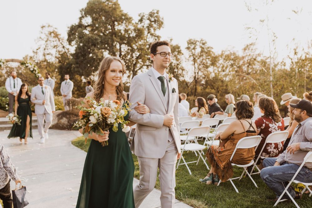 Guests enjoying outdoor wedding reception with white folding chairs at sunset.
