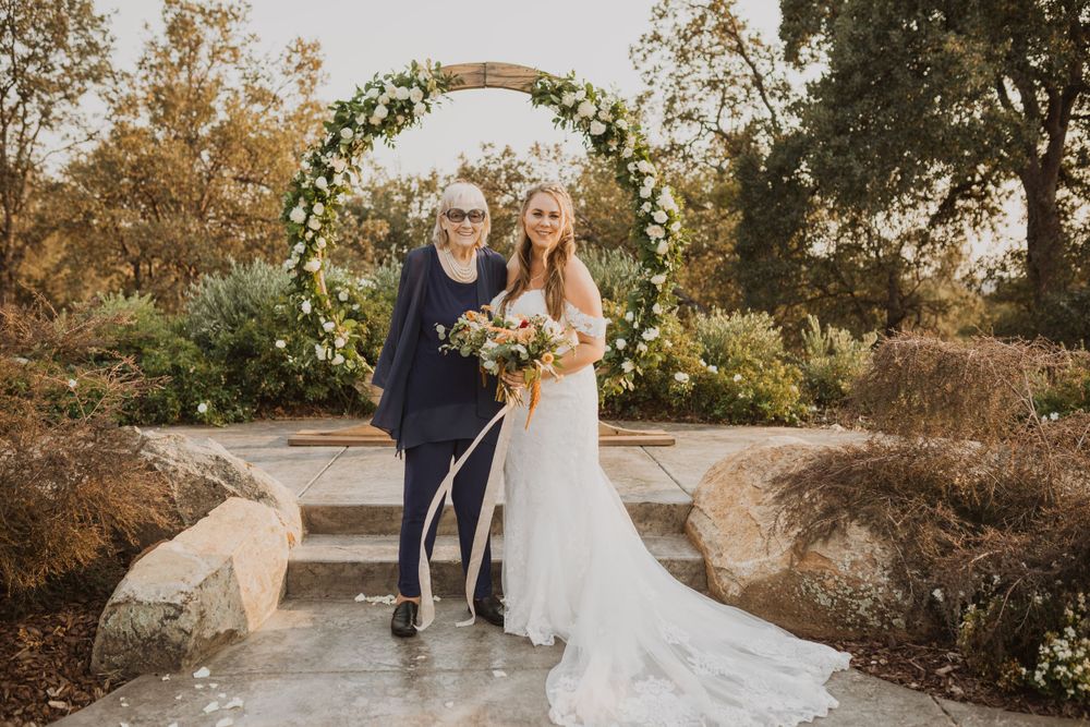 A romantic wedding couple walks together on a path surrounded by autumn trees during golden hour.