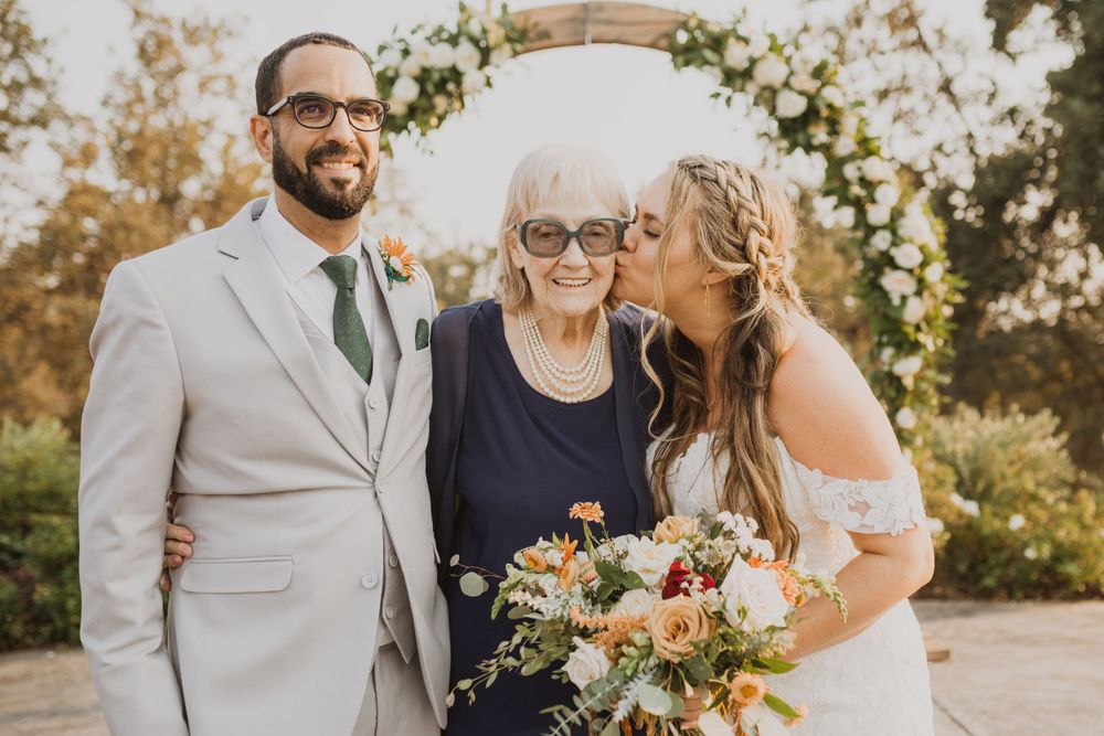 Wedding party gathered under floral arch during outdoor ceremony.