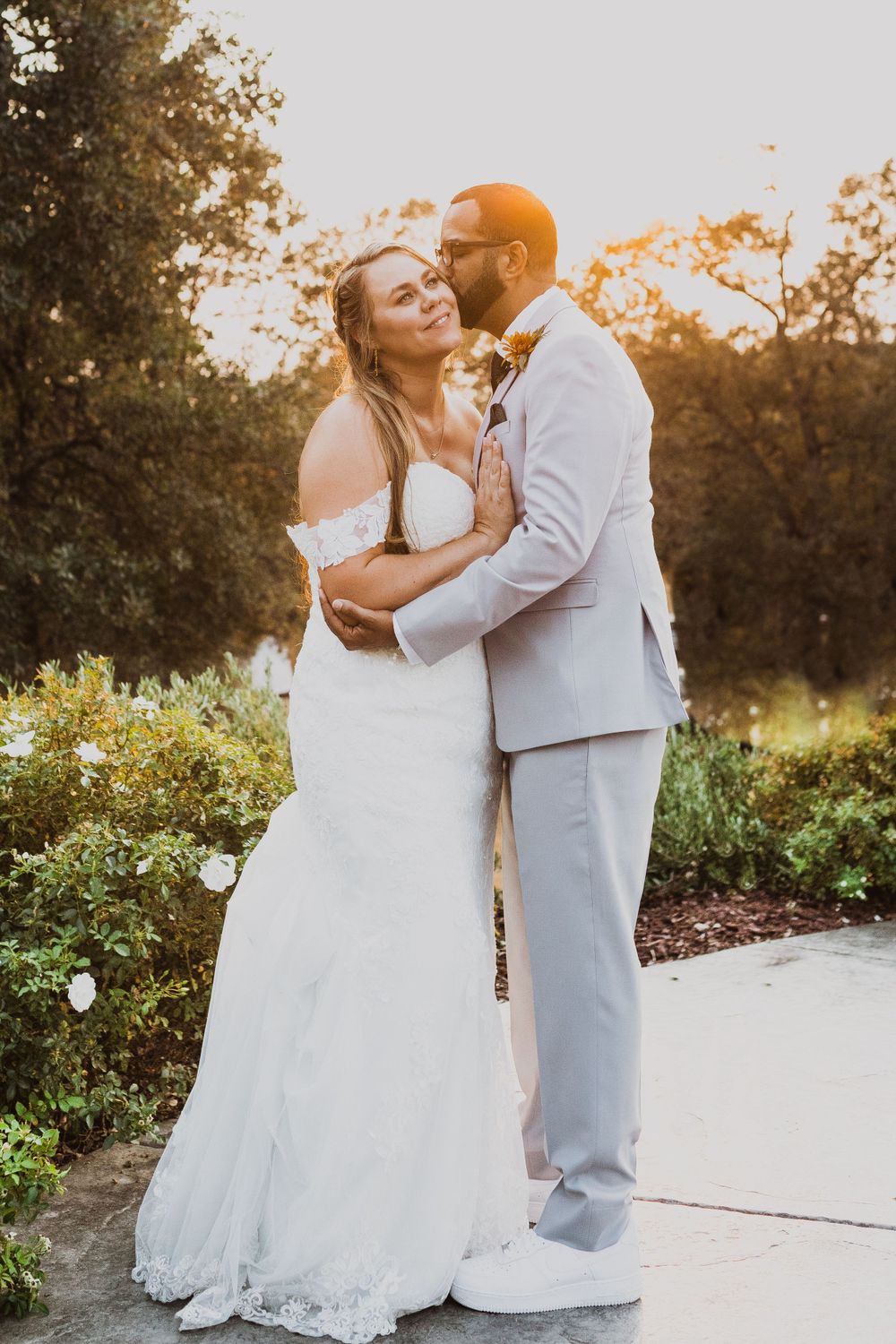 A couple in wedding attire dances and embraces on a paved pathway at sunset.