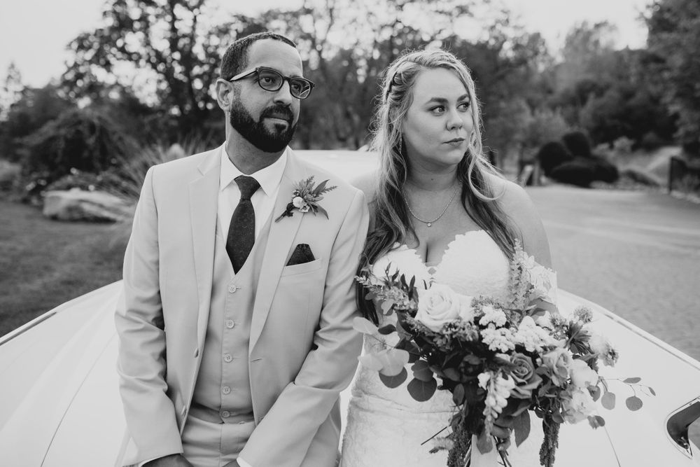 Wedding couple poses for portraits next to classic car in outdoor setting.