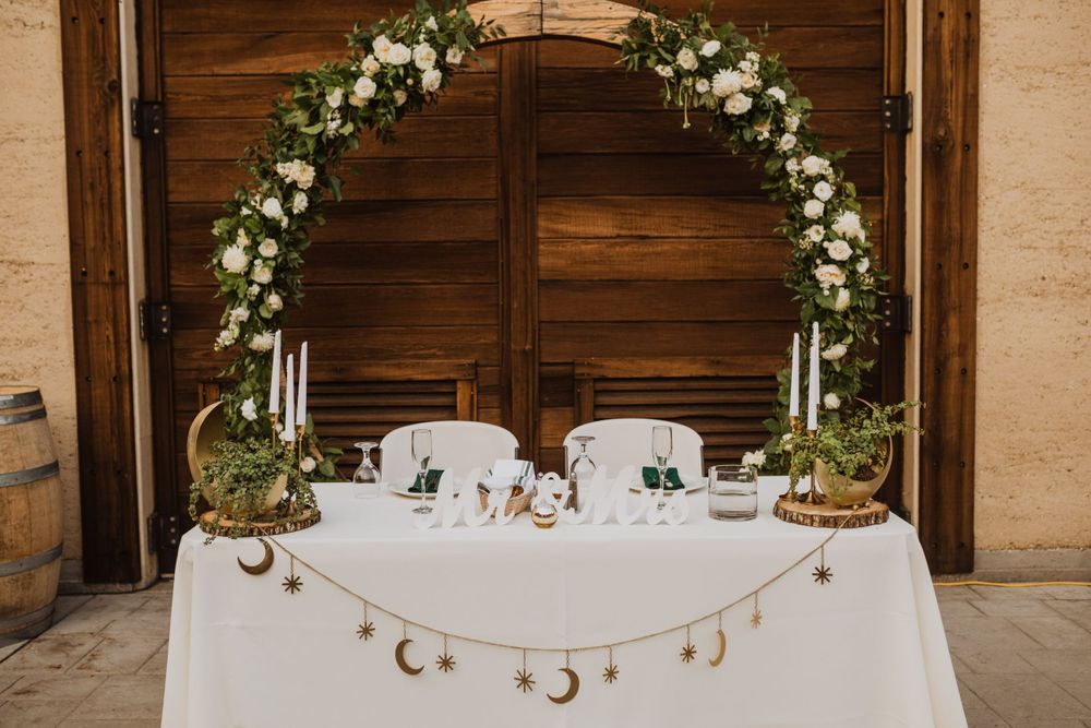 Elegant sweetheart table with floral arch and celestial decorations against wooden backdrop.