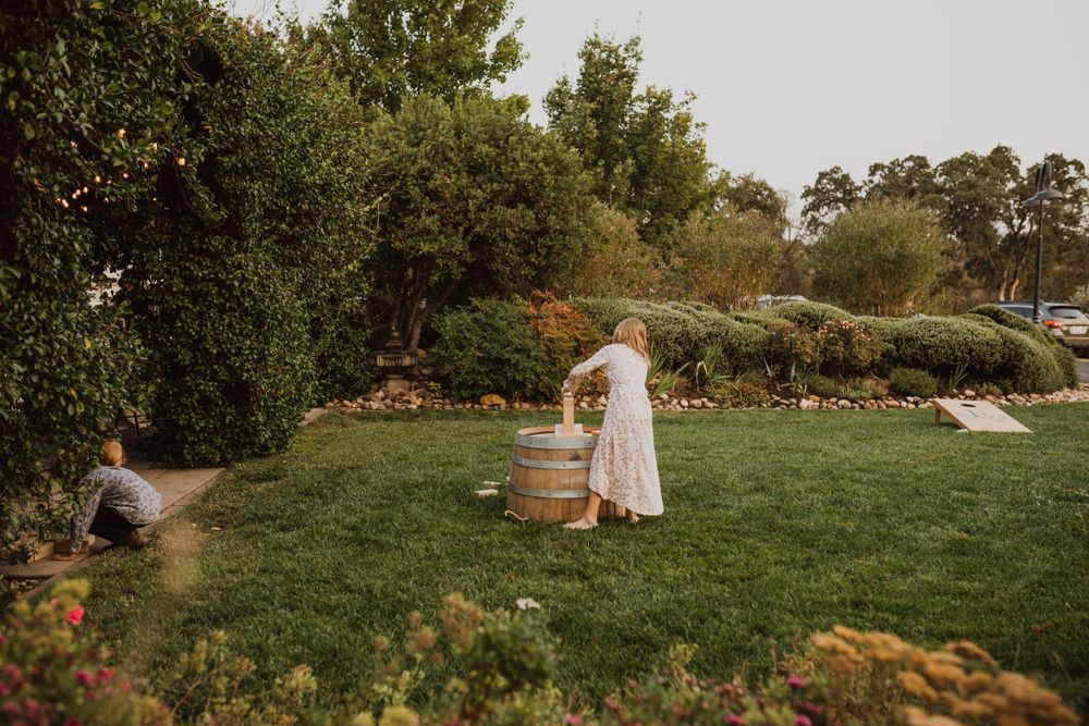 A rustic garden wedding scene with decorative wine barrels and lush greenery in the background.