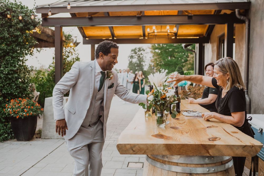 A casual wedding reception moment at a rustic wooden bar under string lights.