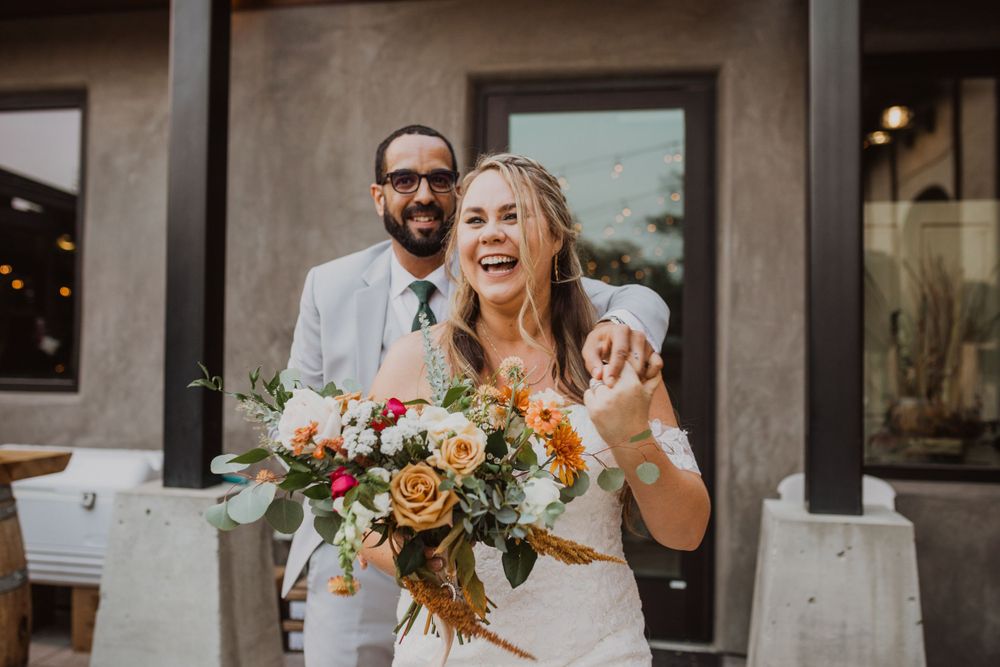 A joyful outdoor wedding moment with autumn-colored bouquet and rustic venue backdrop.