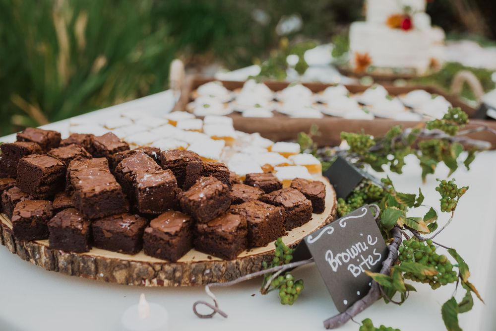 Chocolate brownies displayed on a rustic wood slice platter with greenery at a wedding dessert table.
