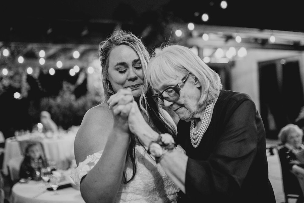 An emotional black and white moment captured during an evening wedding reception with string lights.