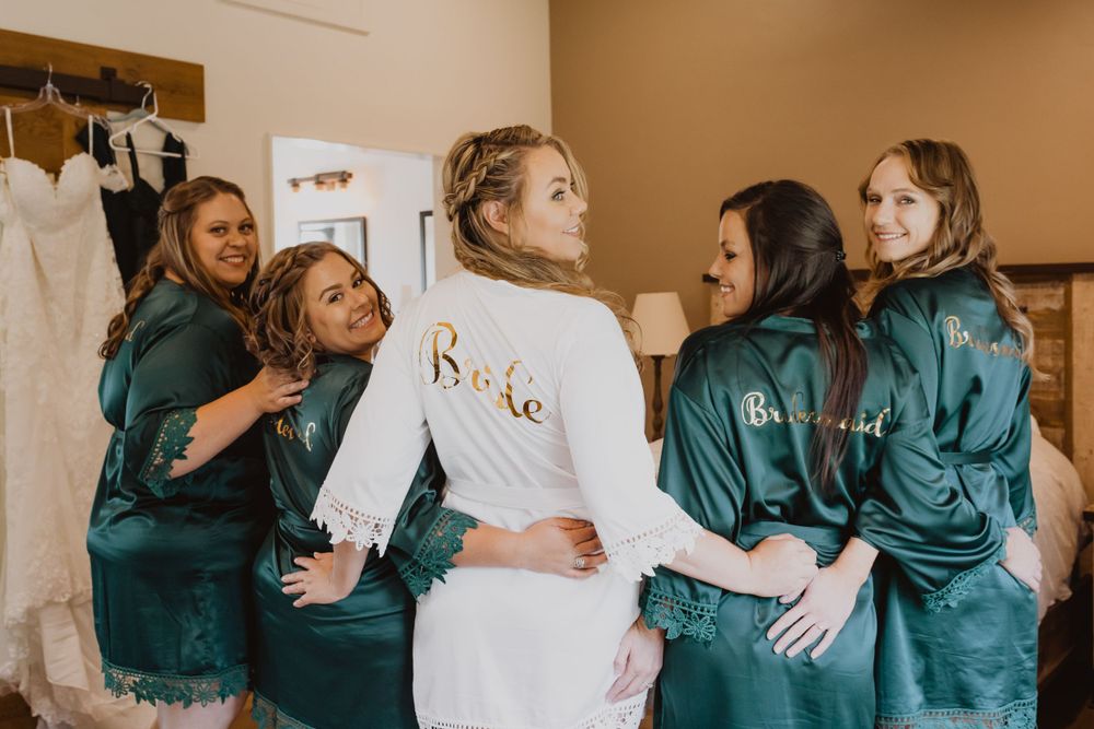 Wedding party members in emerald green robes gather around a white dress.