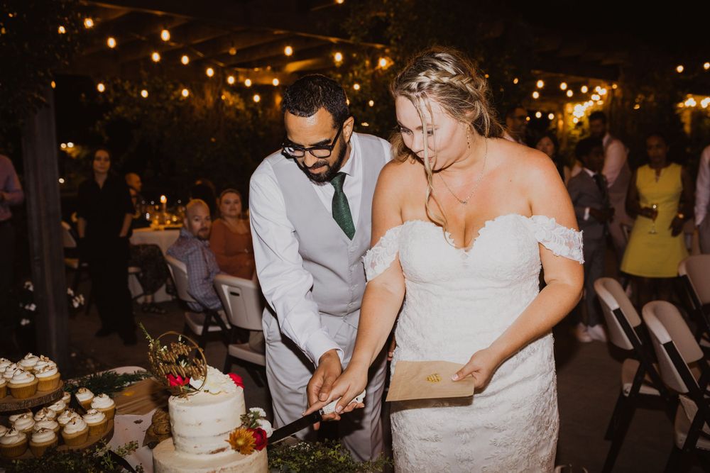 Couple sharing a slice of wedding cake at an evening reception with string lights overhead.