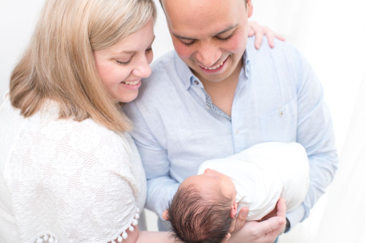 arial shot of dad and mom smiling at their newest newborn baby boy in an all white natural light studio in houston texas