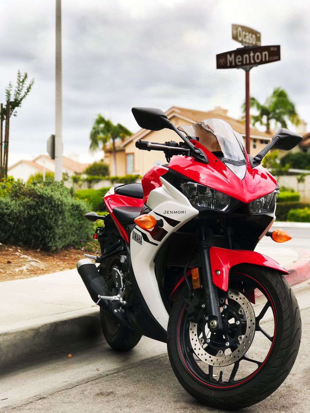 Red and white sport motorcycle parked at street corner intersection in sunny suburban neighborhood.