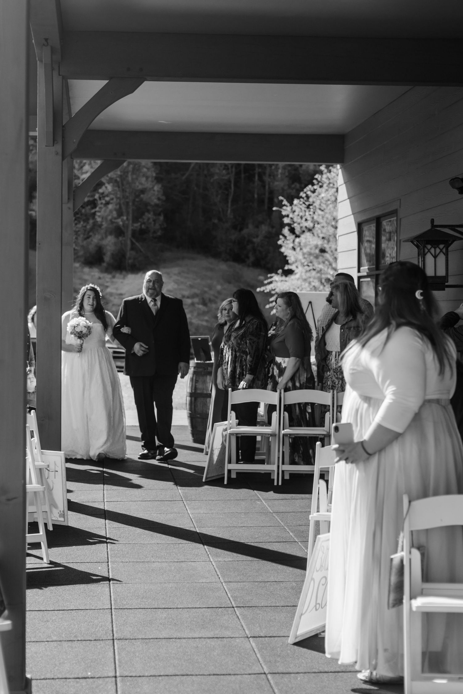 Black and white photo of a wedding ceremony setup with guests gathering under a covered pavilion.