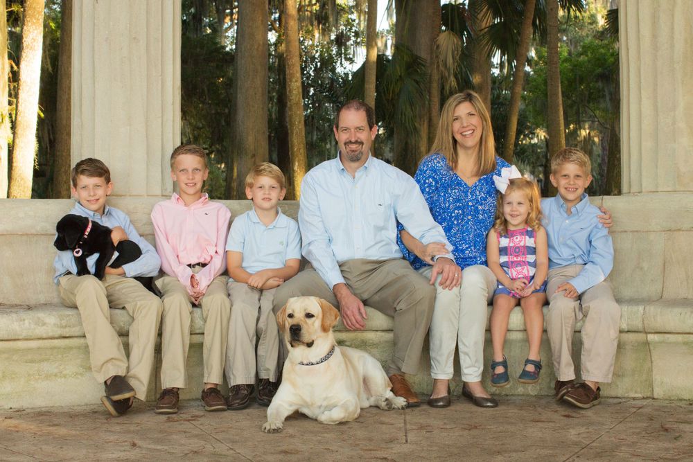 A family poses together on stone steps with their golden retriever in a sunny outdoor setting.