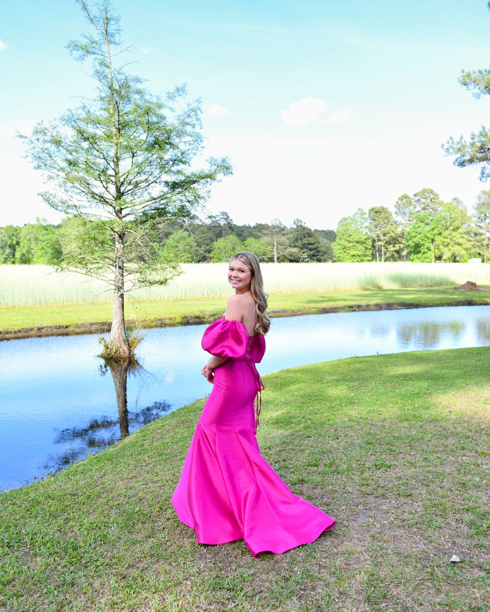 Elegant formal dress photo by a lake with a bright pink gown against natural scenery.