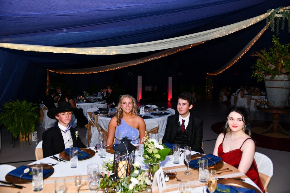 Formal dinner setting under blue tent with decorated tables and guests enjoying a meal.
