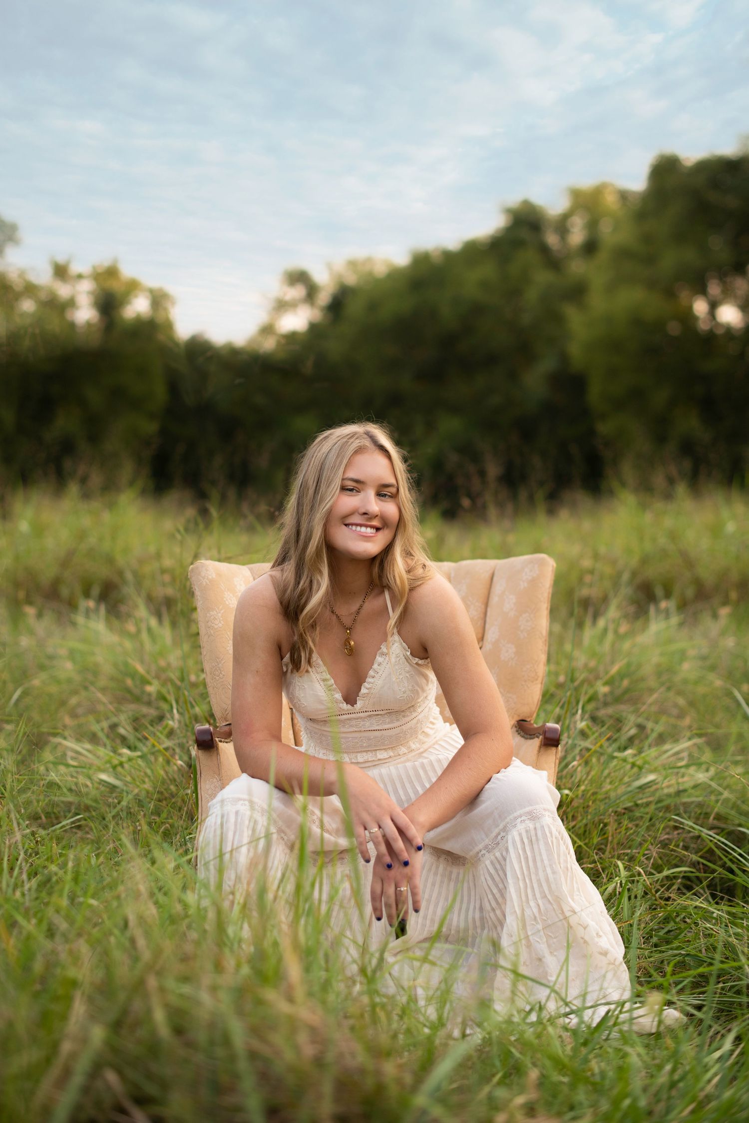 Person in white dress sitting on tan chair in tall grass during golden hour.
