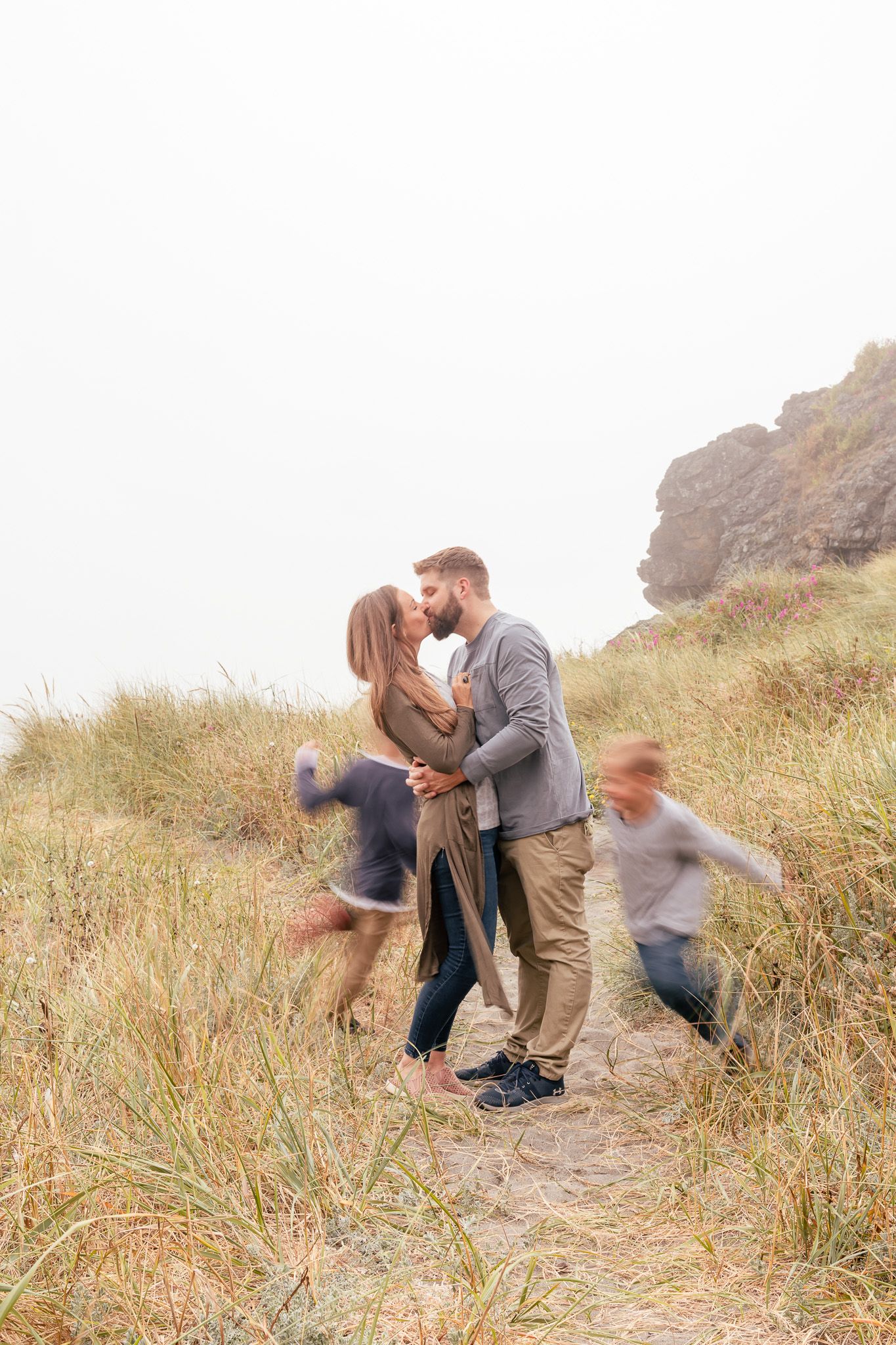 Couple kissing while photographer captures children excitedly running circles around their parents.