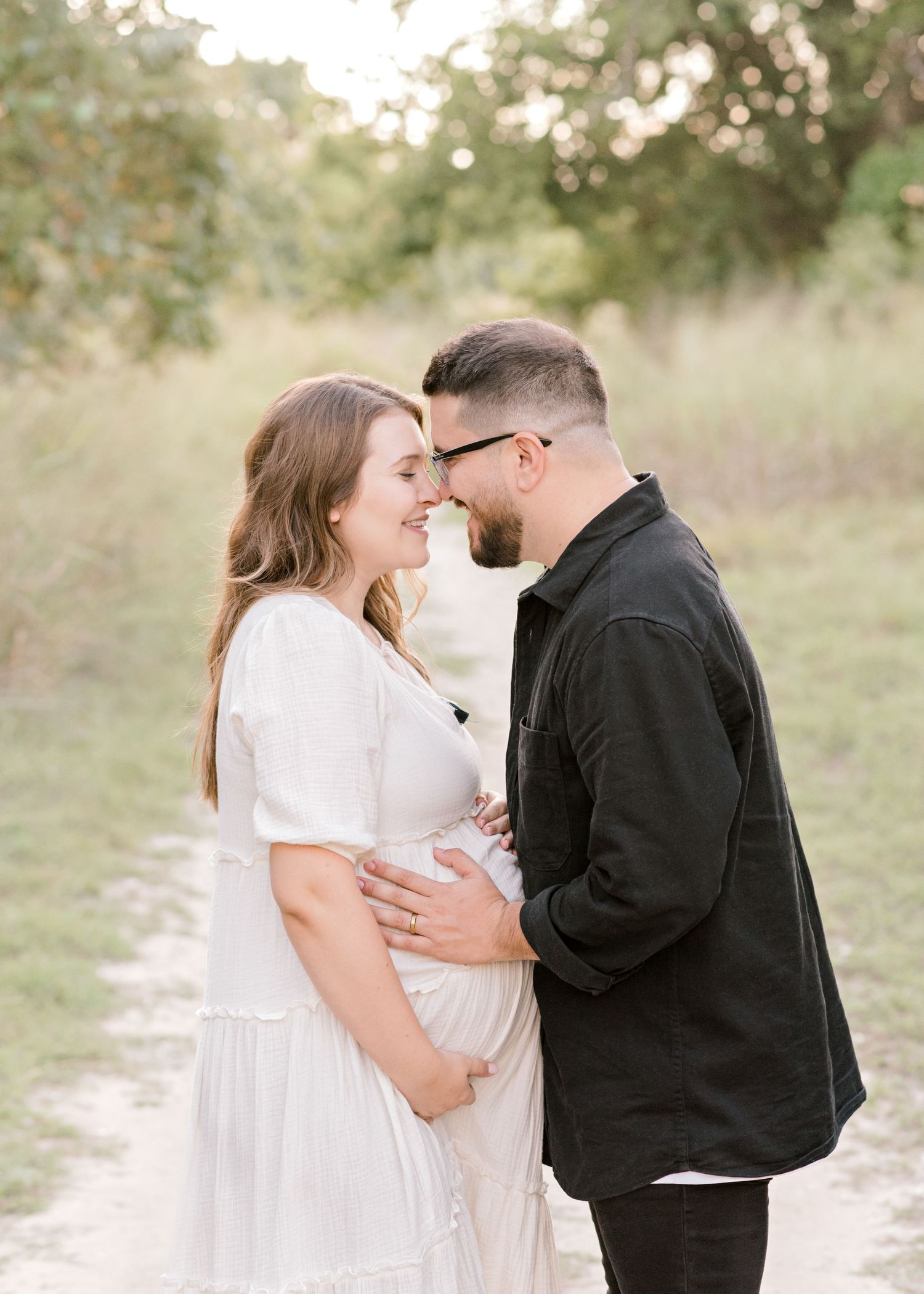 husband and wife facing each other going nose to nose as they both hold onto her baby bump in Austin, TX
