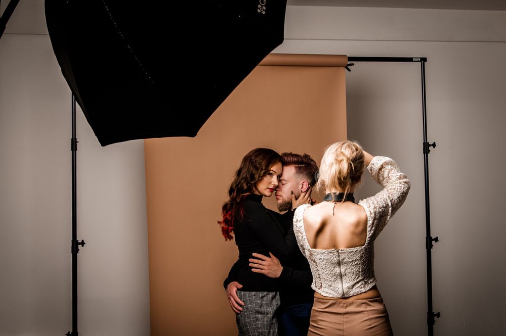 Behind the scenes studio photo of couple posing intimately with lighting equipment visible.