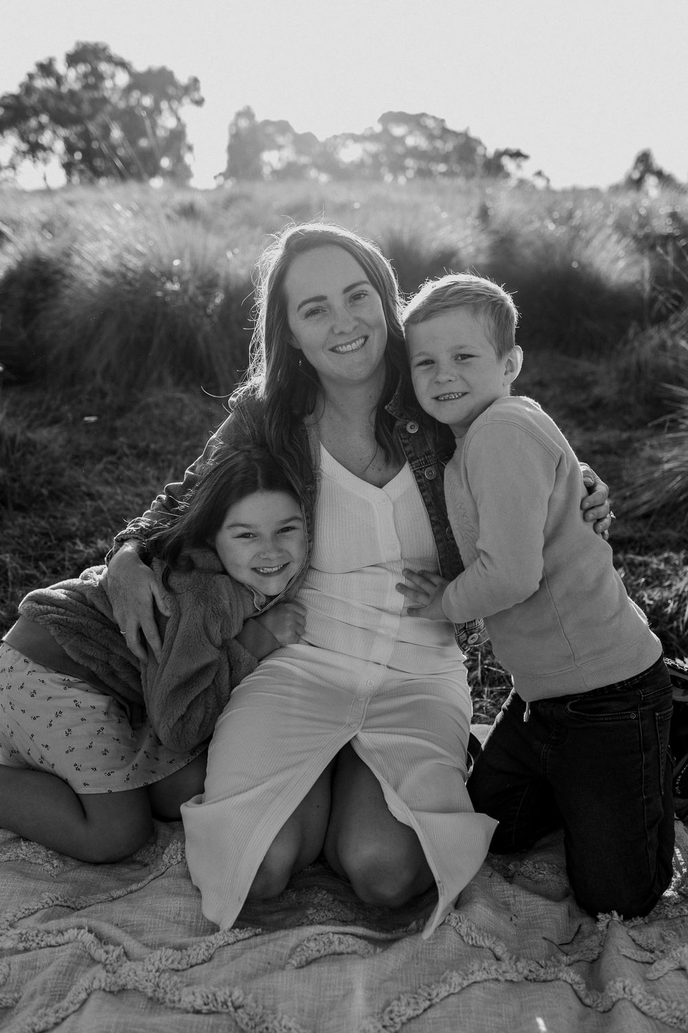 Black and white portrait of people sharing a tender moment together outdoors on a blanket in natural lighting.