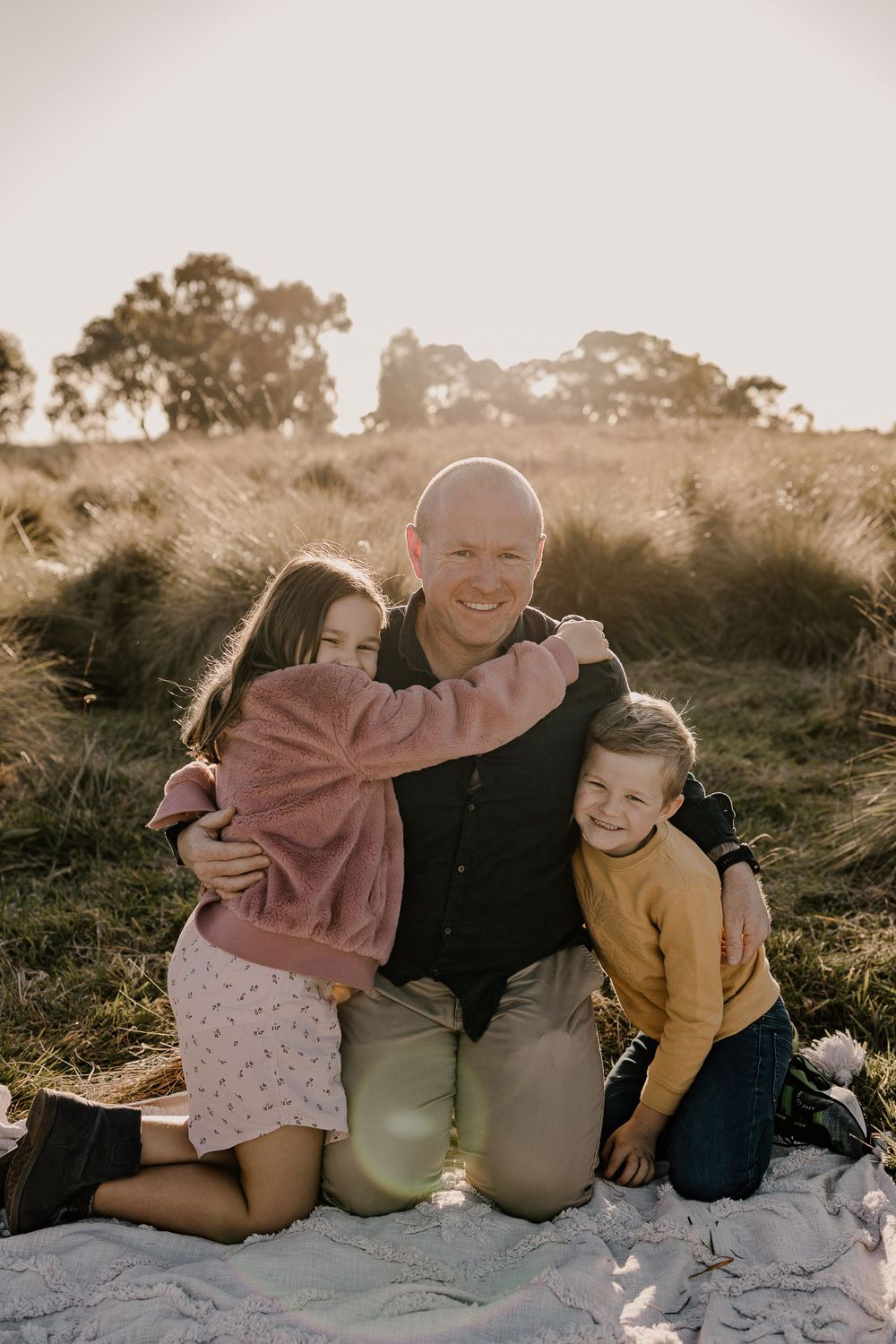 A joyful candid family embrace captured in warm sunlight among tall grasses.
