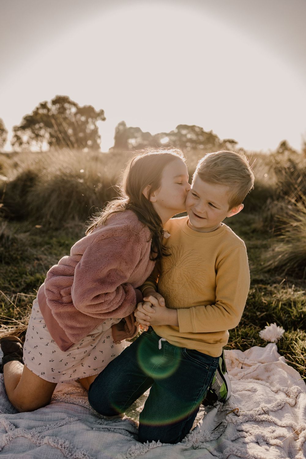 Two children sharing a sweet moment together on a blanket during sunset.