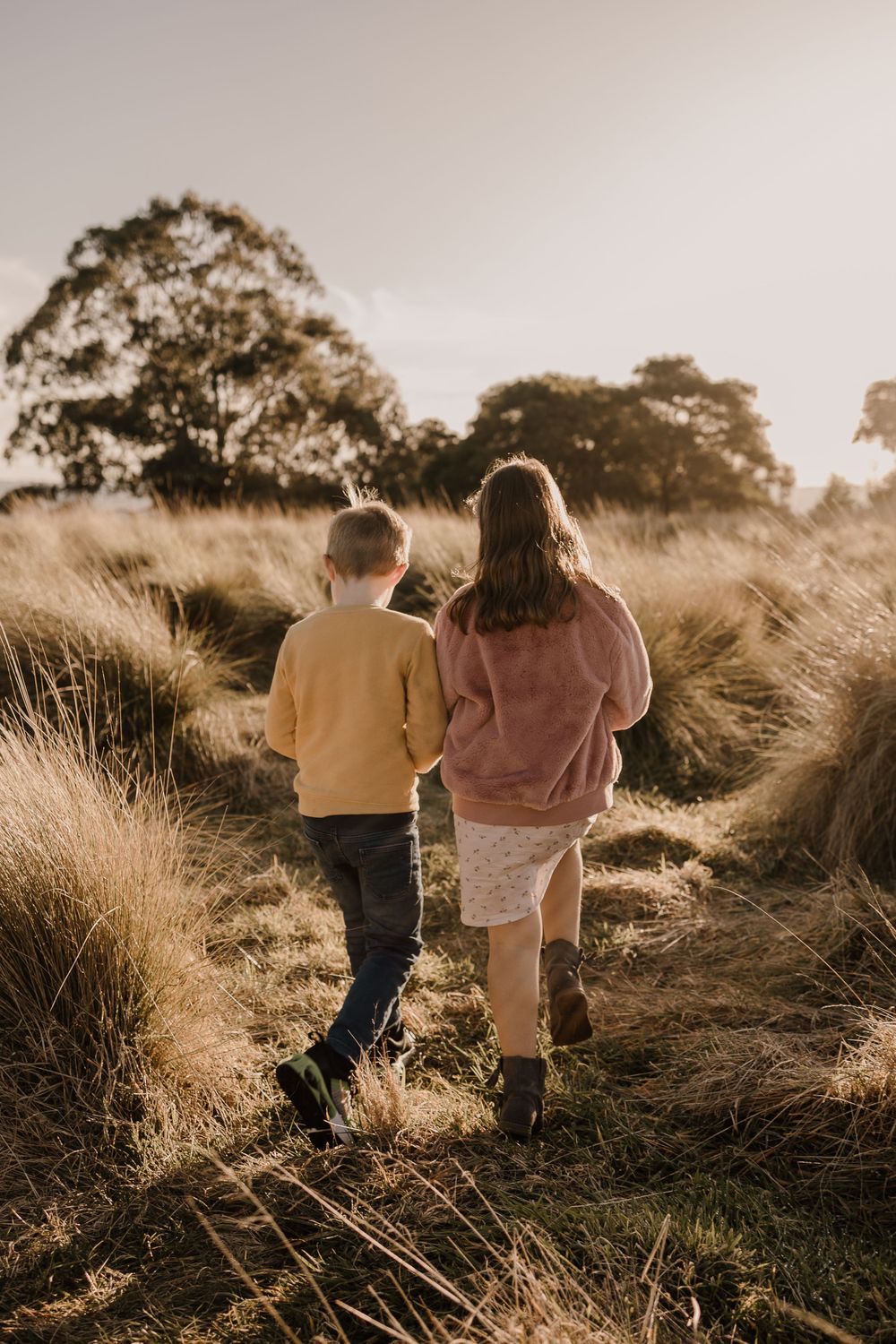 Two figures walking together on a sunlit path through tall grass.