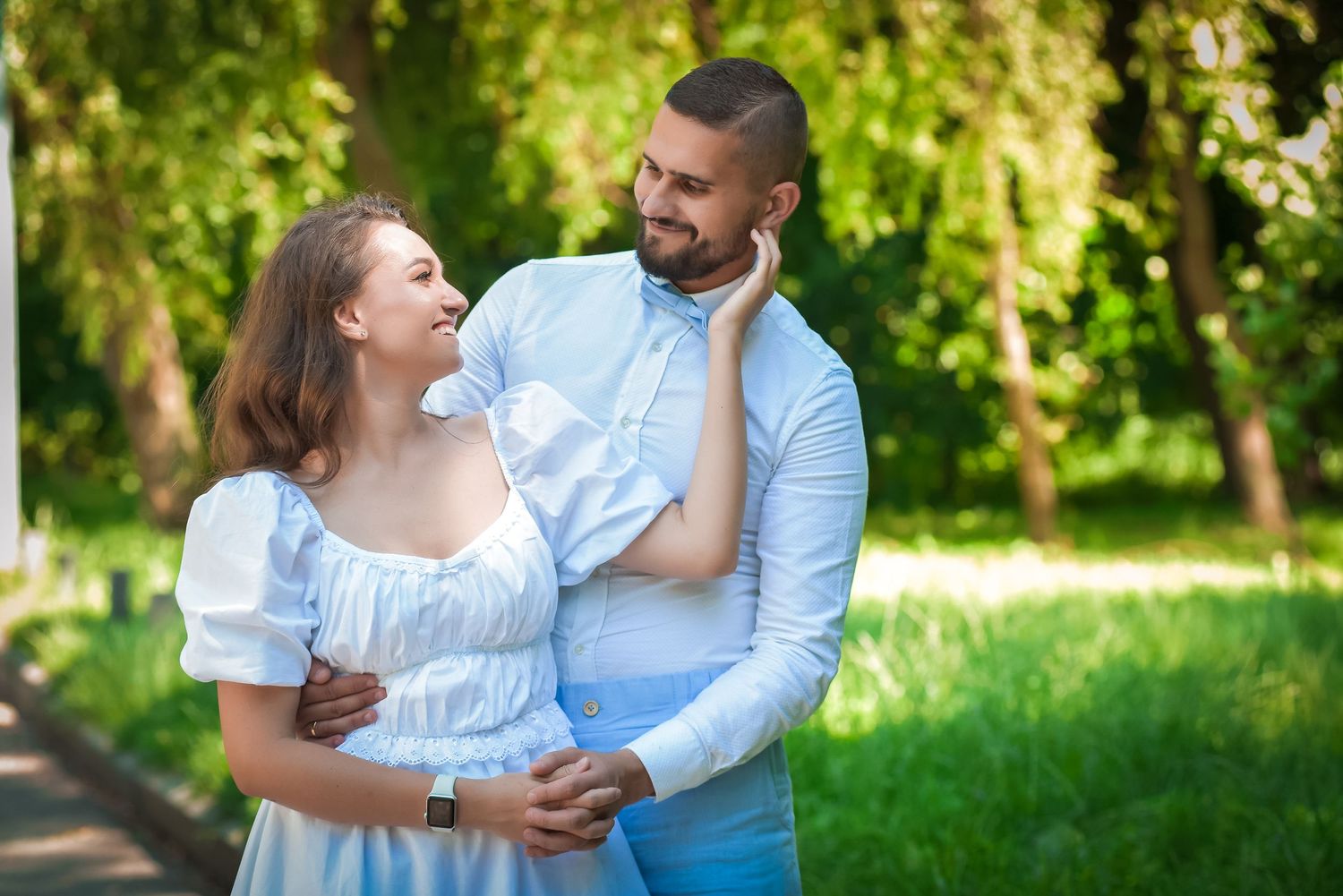 Couple in white and blue outfits sharing tender moments in sunny garden setting.