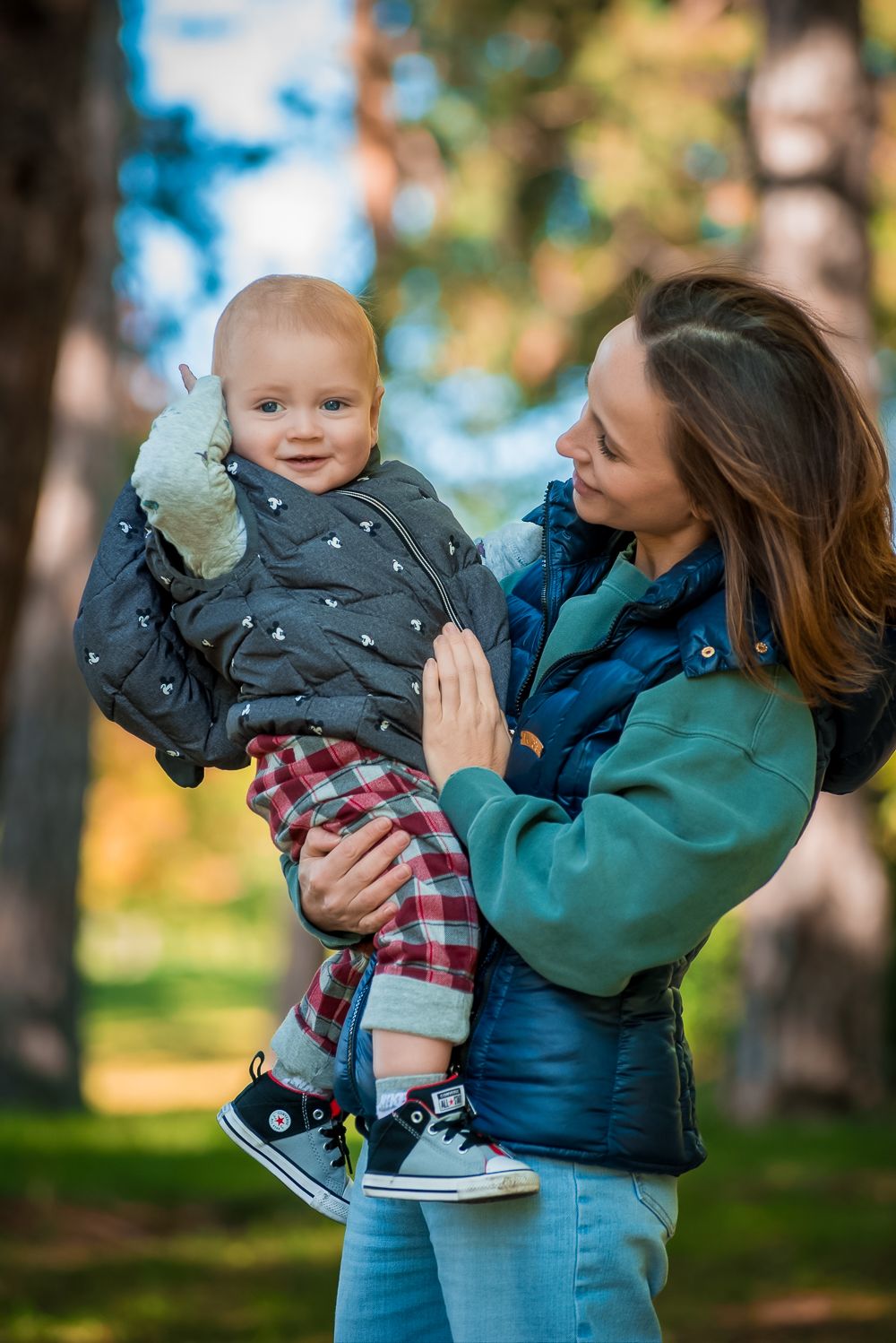A toddler in plaid pants and winter jacket shares a joyful moment with parent in an outdoor setting.
