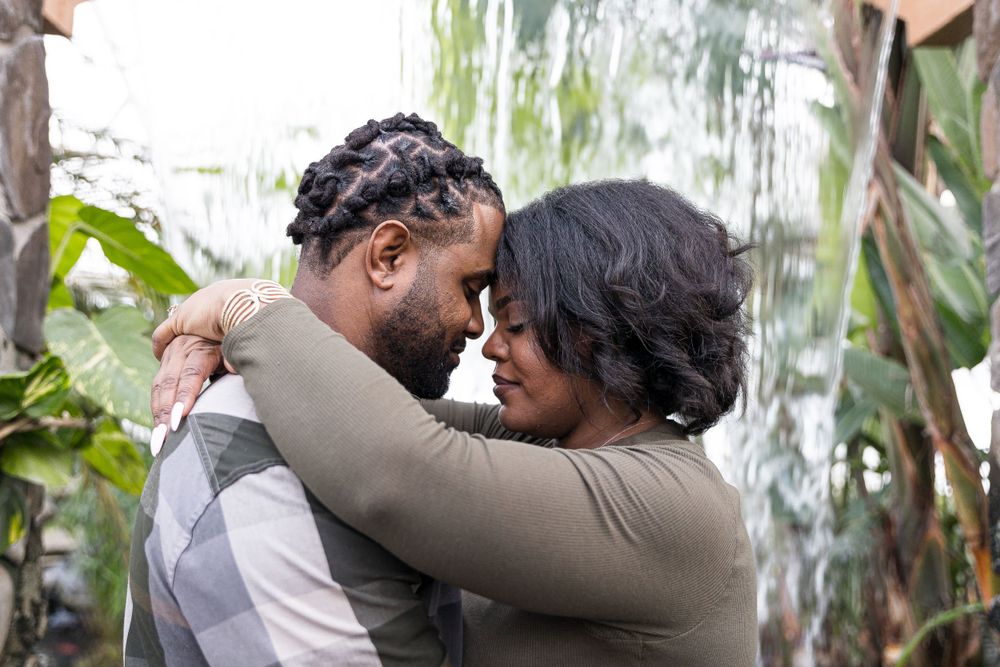 A tender moment between a couple embracing outdoors with a weeping willow tree in the background.