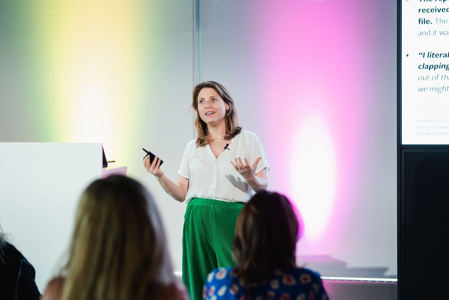 Speaker presents to audience in modern conference room with colorful gradient lighting on walls.