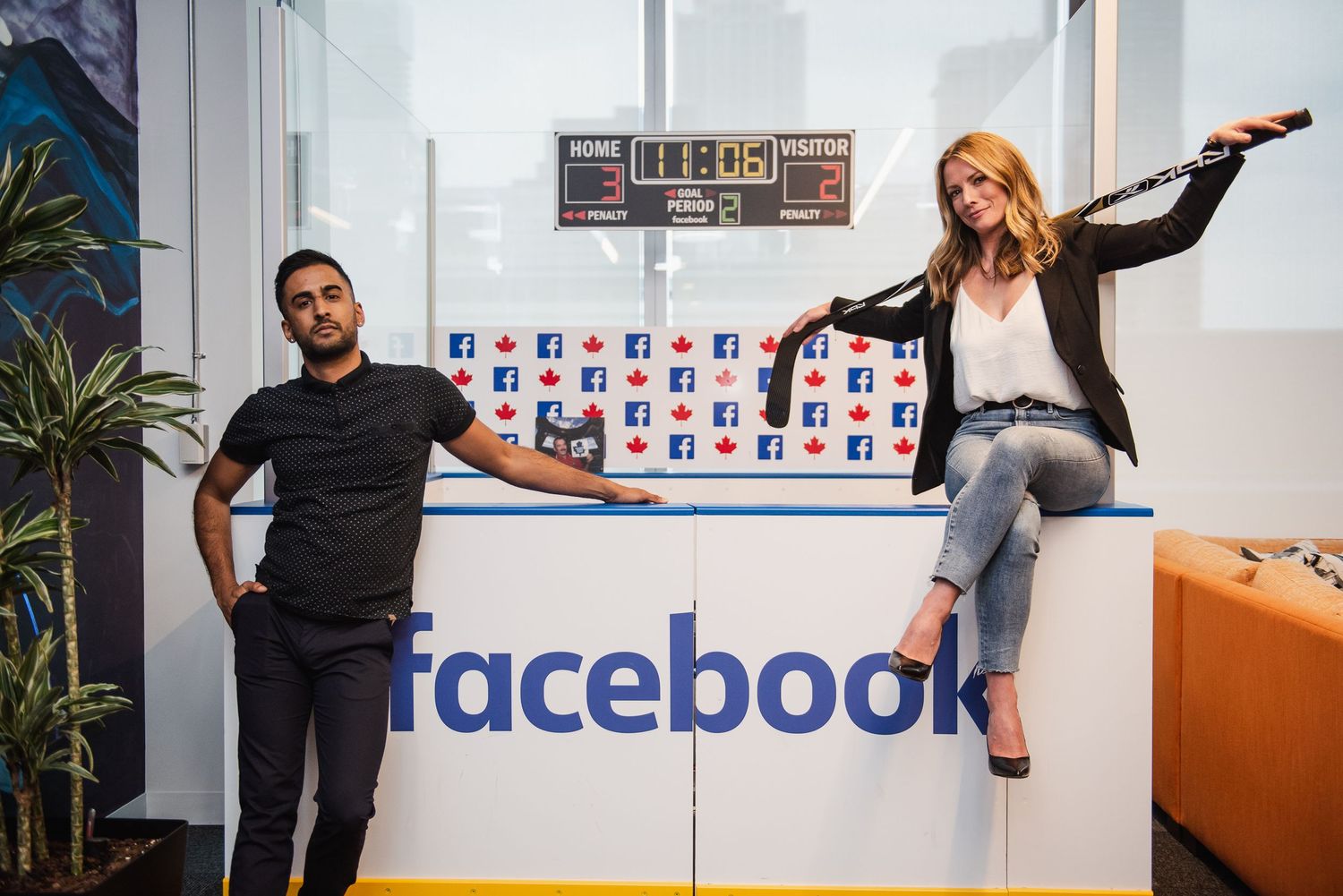 Two people pose playfully by Facebook logo in modern office space.