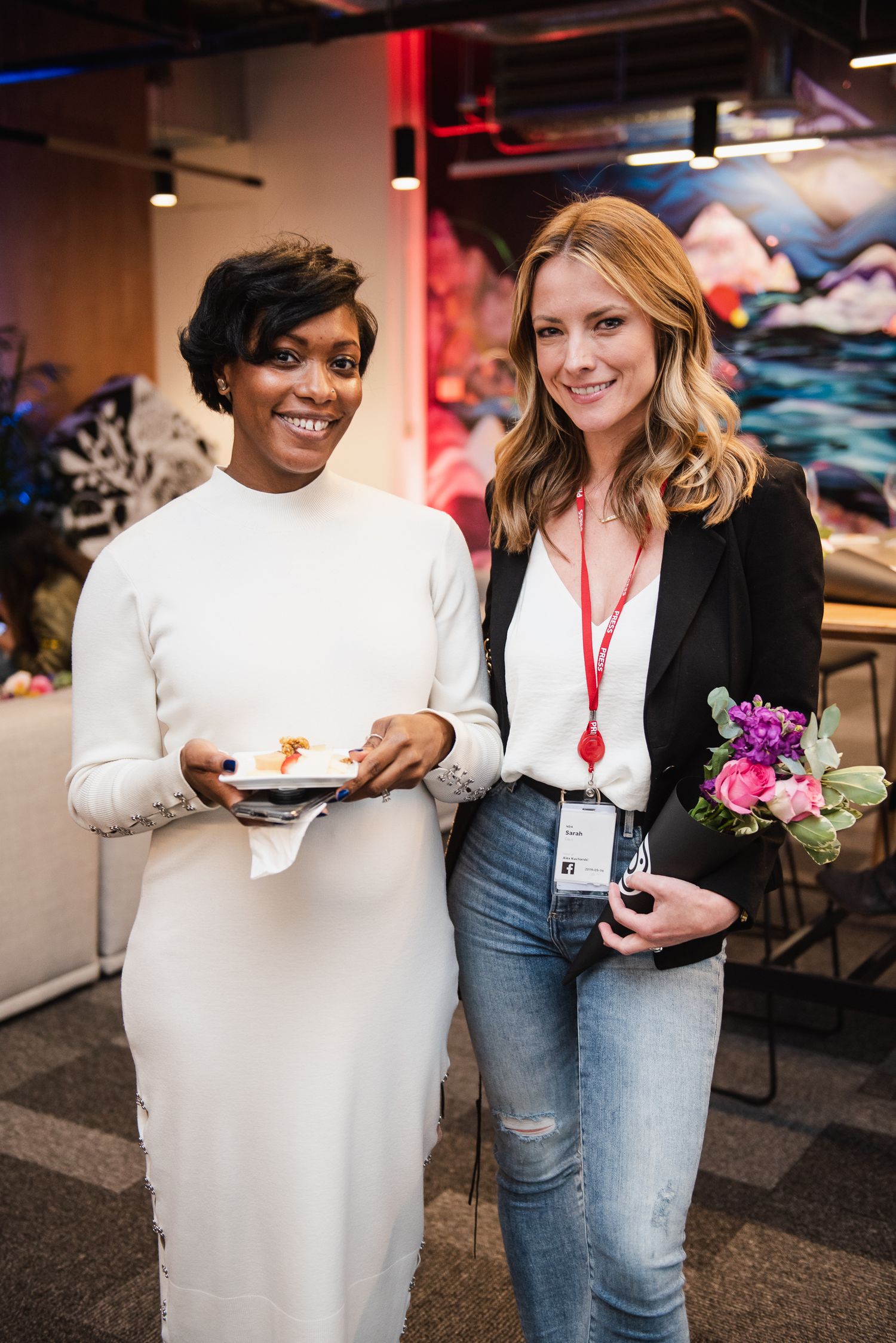 Two professionals smile while holding items at a casual business networking event.