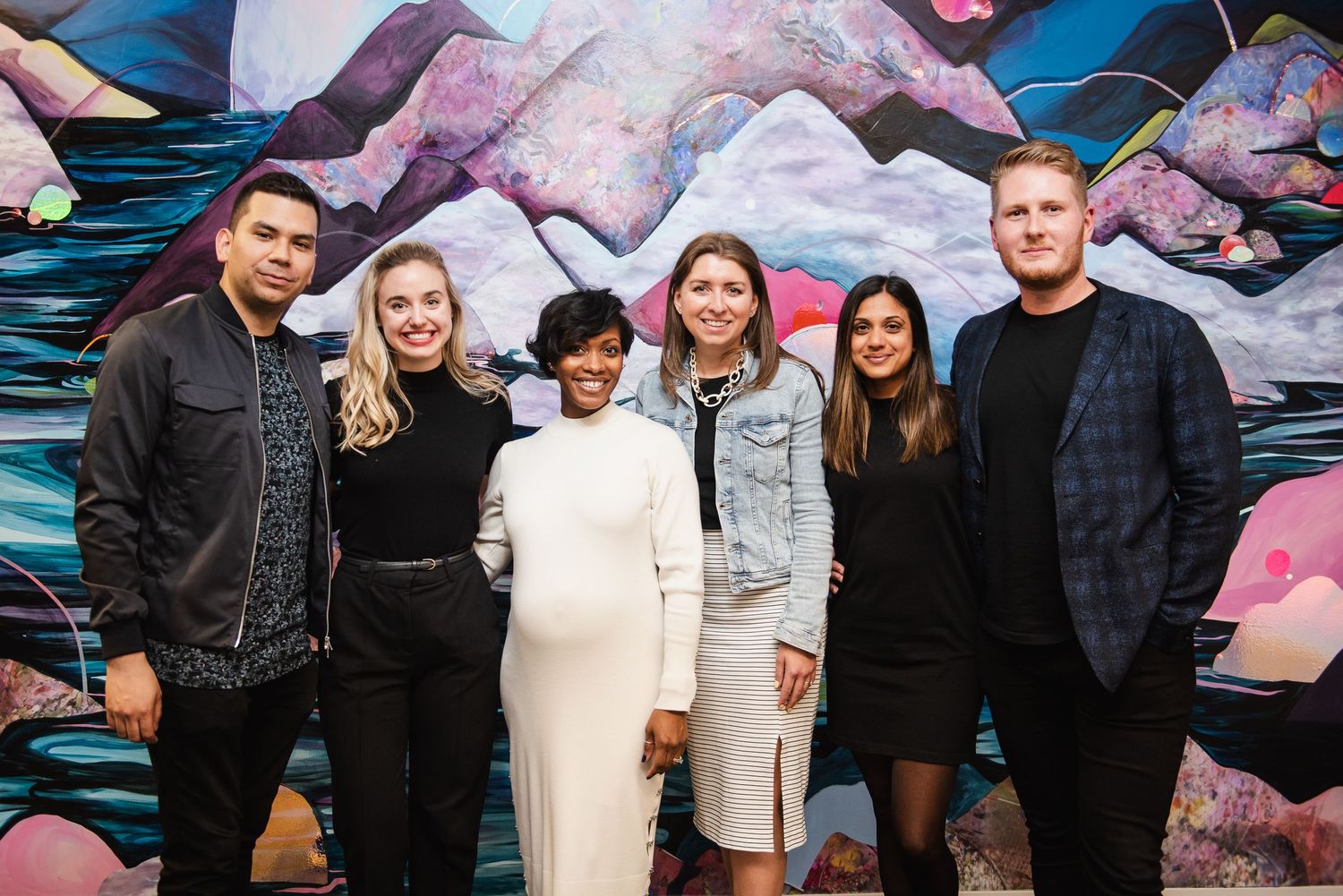 Group of professionals poses together in front of artistic wall mural at business event.