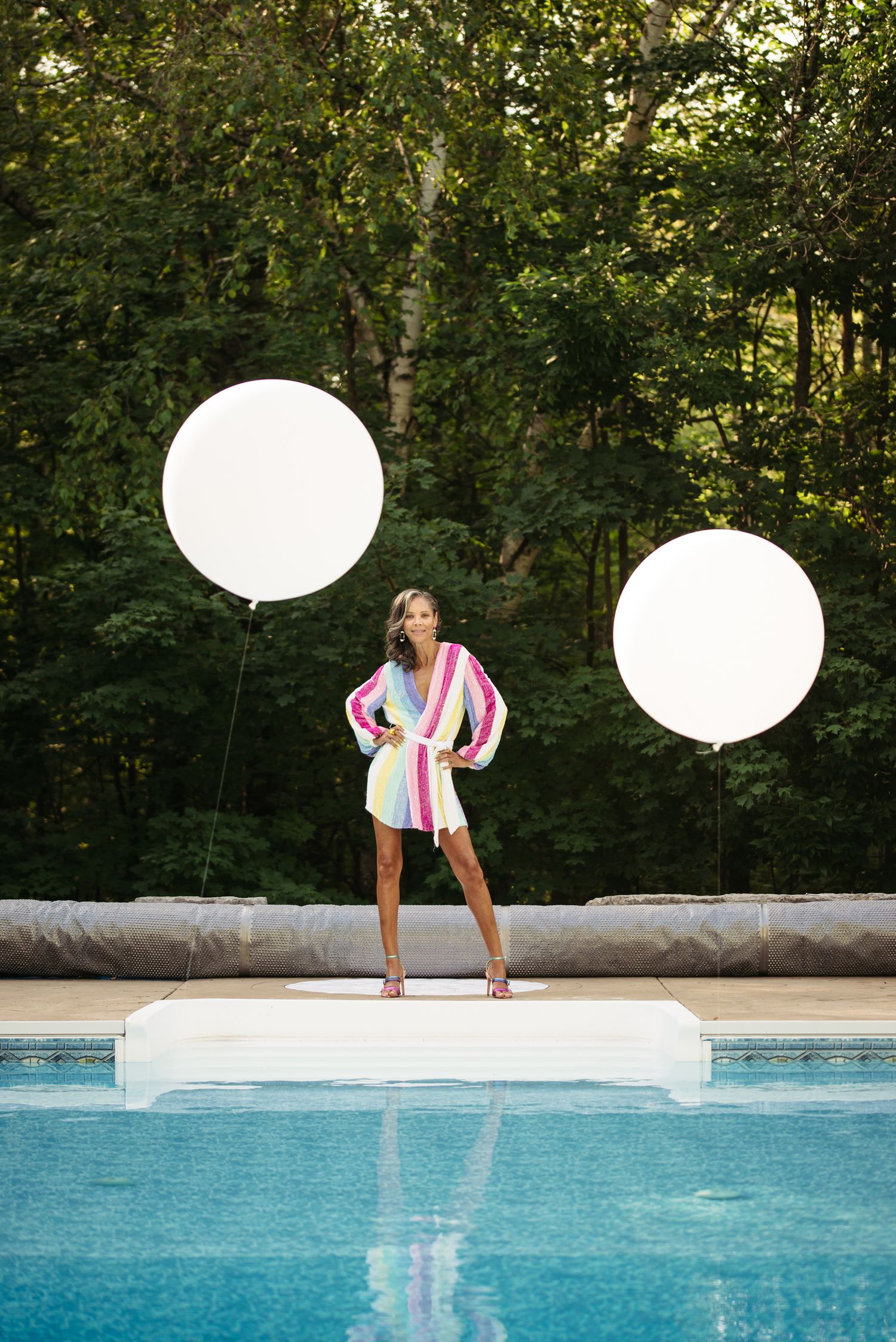 A colorful poolside scene with large white balloons and a swimming pool in a garden setting.