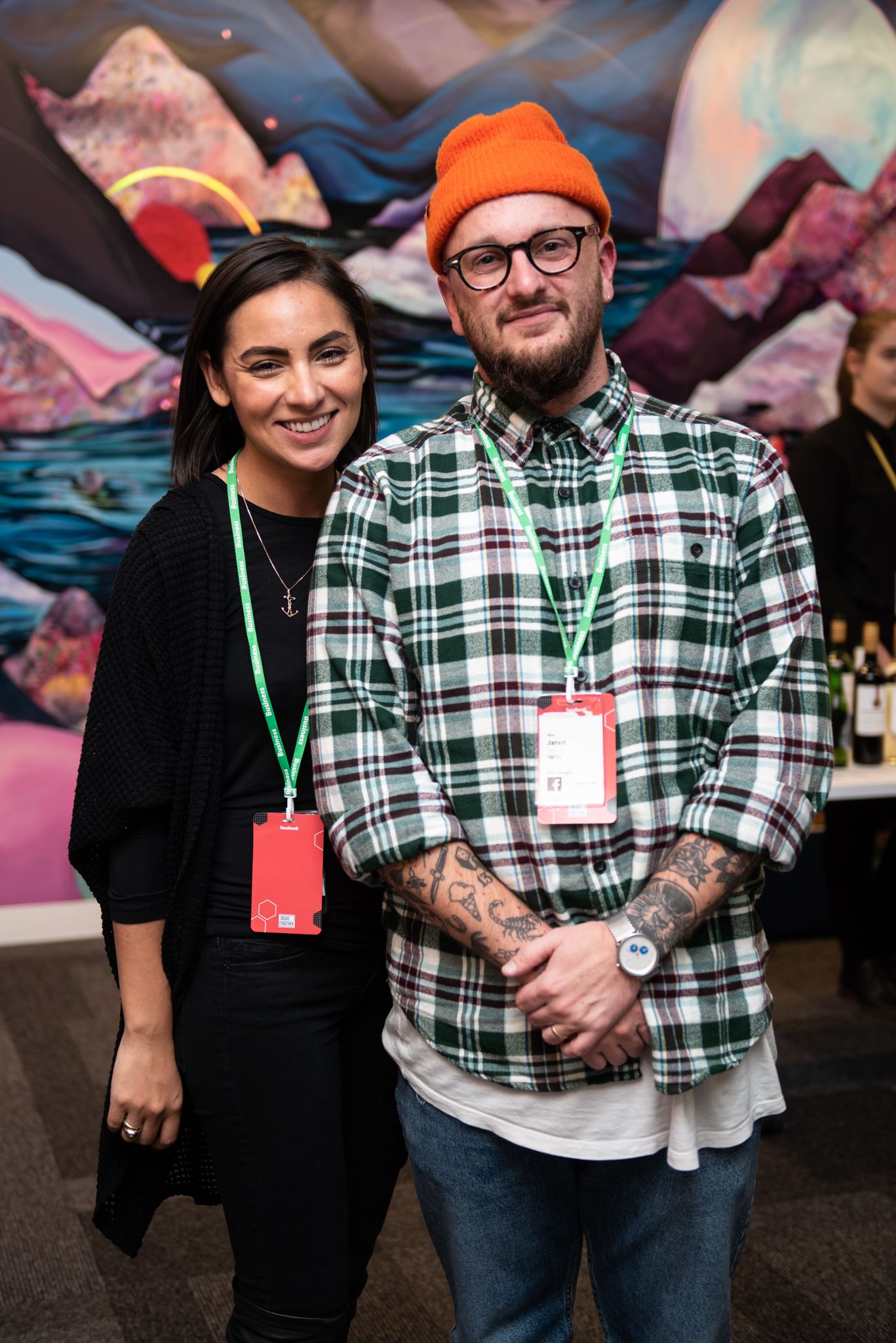 Two attendees posing at a conference in front of colorful wall art.