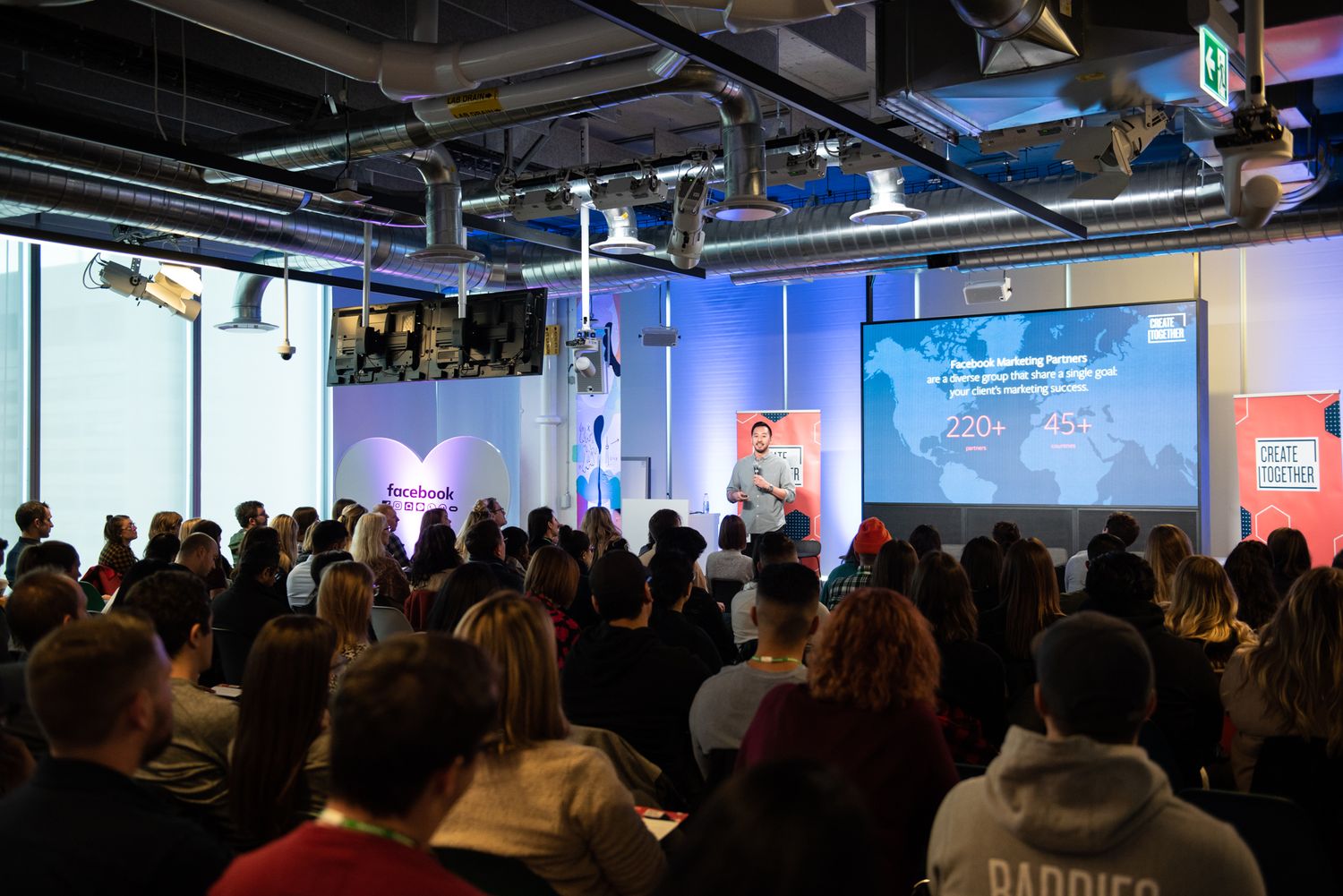 Large audience attending a conference presentation in modern venue with blue lighting.