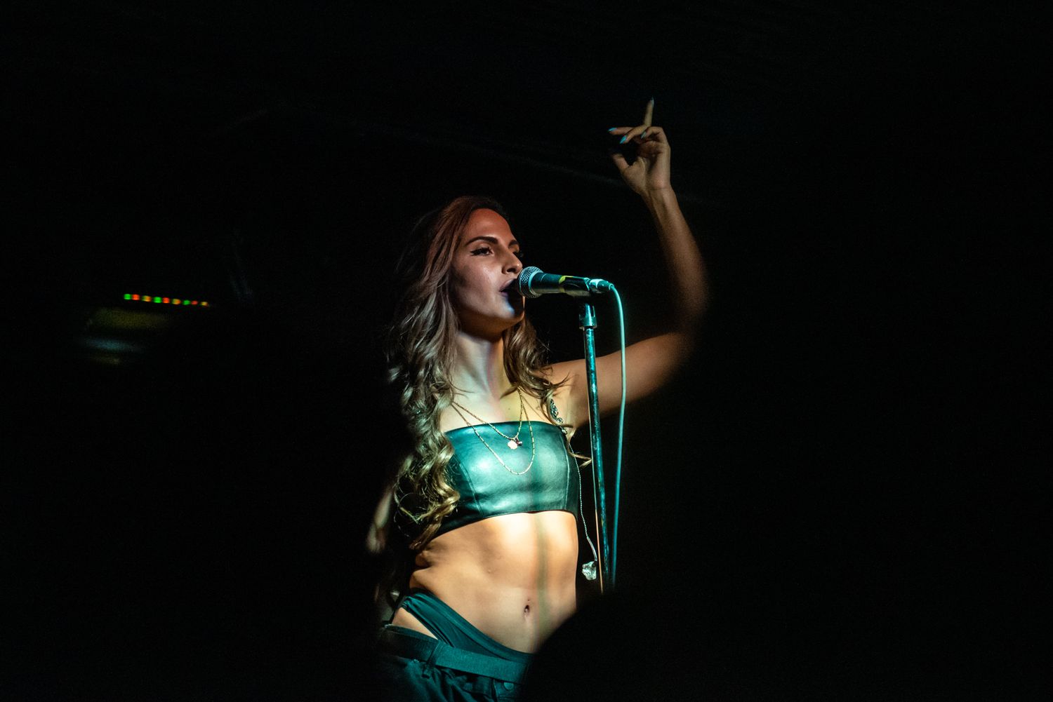 A performer in a turquoise outfit sings passionately on stage under dramatic lighting.