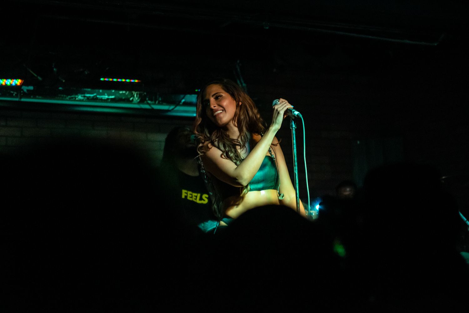 A performer sings emotively into a microphone on a dimly lit stage.