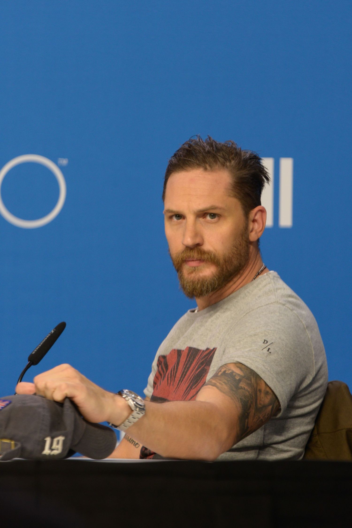 Man in grey t-shirt with beard signs autographs at press conference.