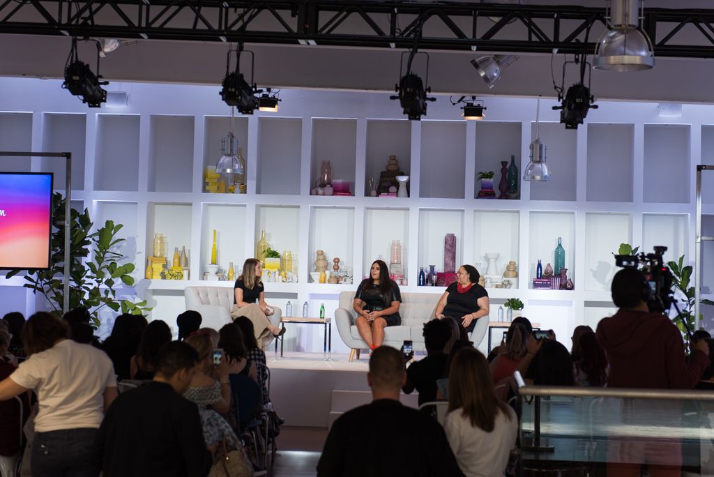 Event stage setup with studio lighting and white shelving displaying products to an audience.