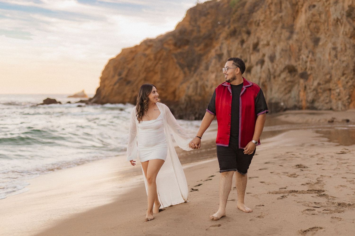 Couple walking hand in hand on scenic beach at sunset.