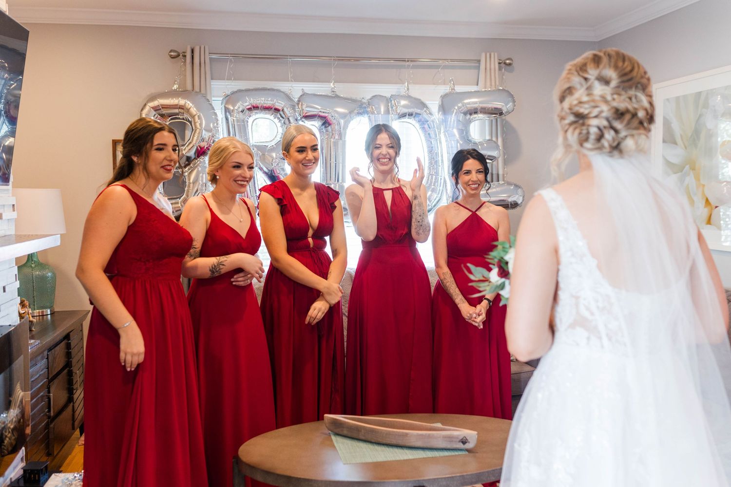 Bridesmaids in matching crimson dresses share joyful moment with bride in wedding dress.